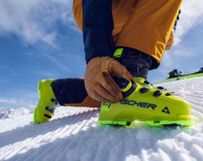 Sciatore allaccia scarponi gialli su pista innevata.